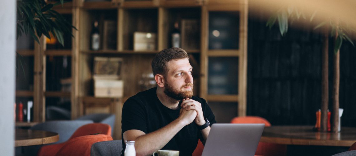 Bearded man sitting in a cafe drinking coffee and working on a computer
