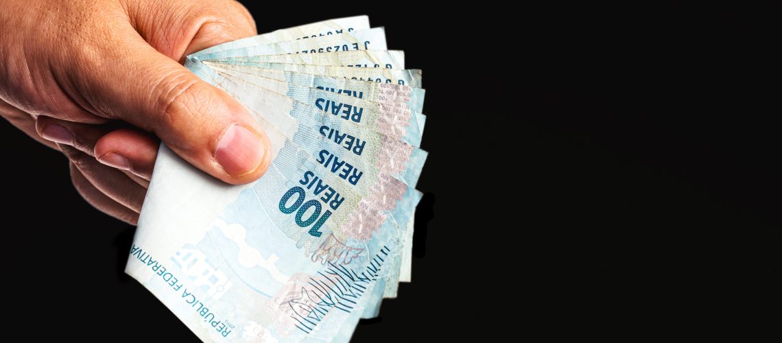 hand holding several hundred reais bills from Brazil, on isolated black background. Emergency government aid paid to microentrepreneurs, worth 600 reais